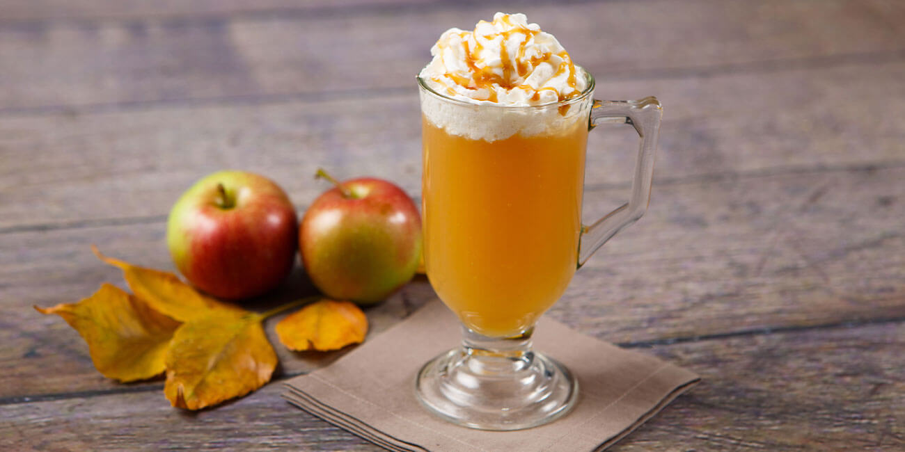 Hormel Health Labs thickened caramel hot toddy in a tall glass on a table in front of apples